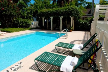 A clear swimming pool with green lounge chairs and neatly rolled towels beside it.