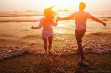 A couple joyfully runs hand in hand along the beach at sunset.