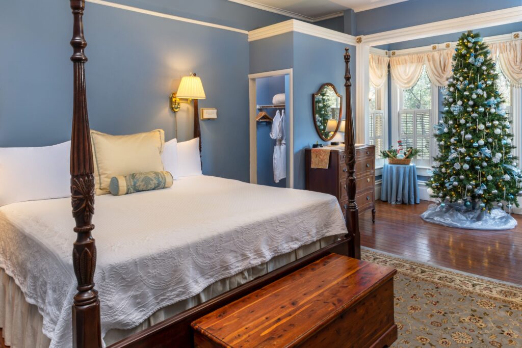A cozy bedroom featuring a four-poster bed, a decorative Christmas tree, and warm blue walls.