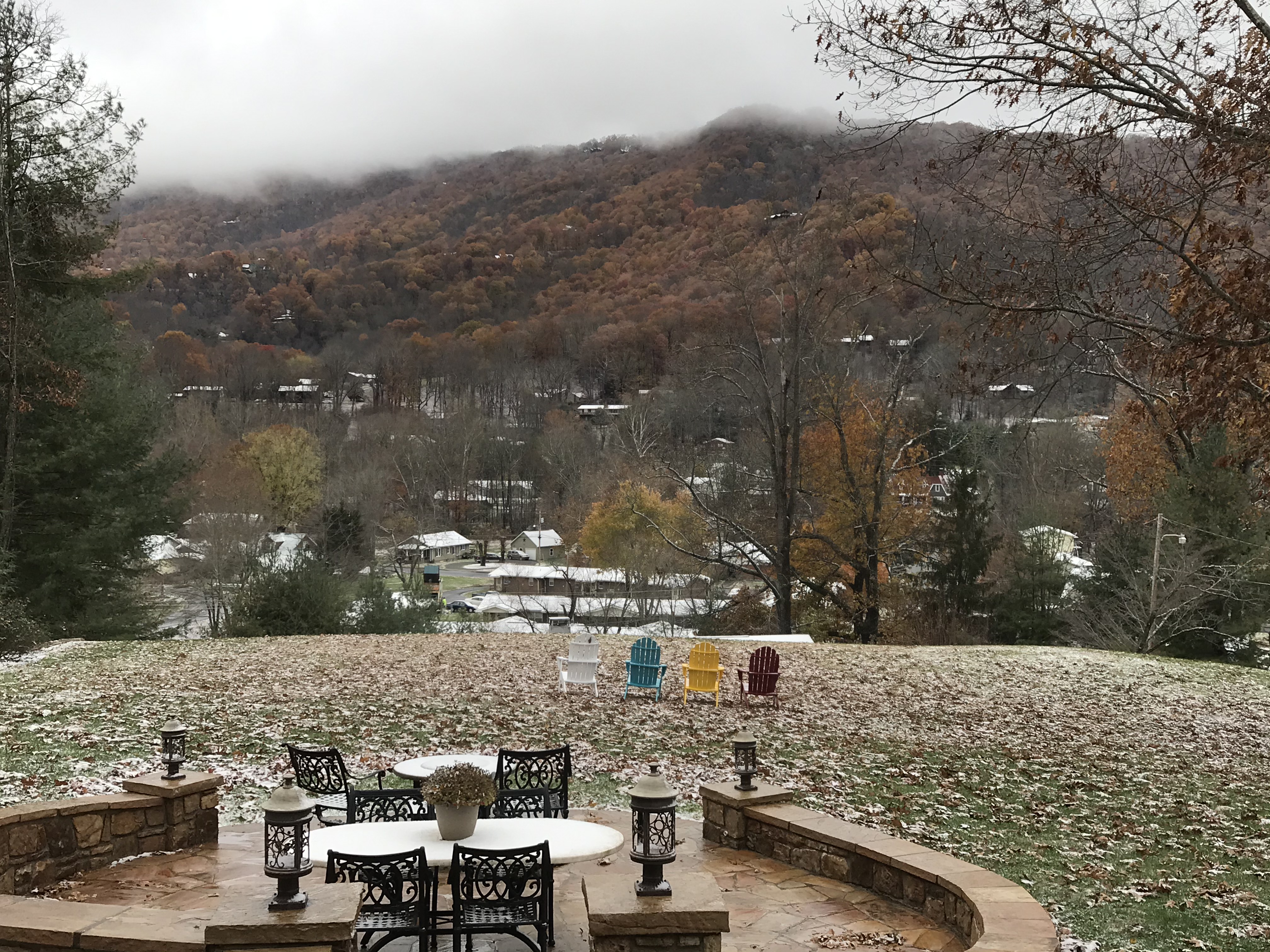 A landscaped yard with colorful chairs overlooks a misty, autumnal mountain view.