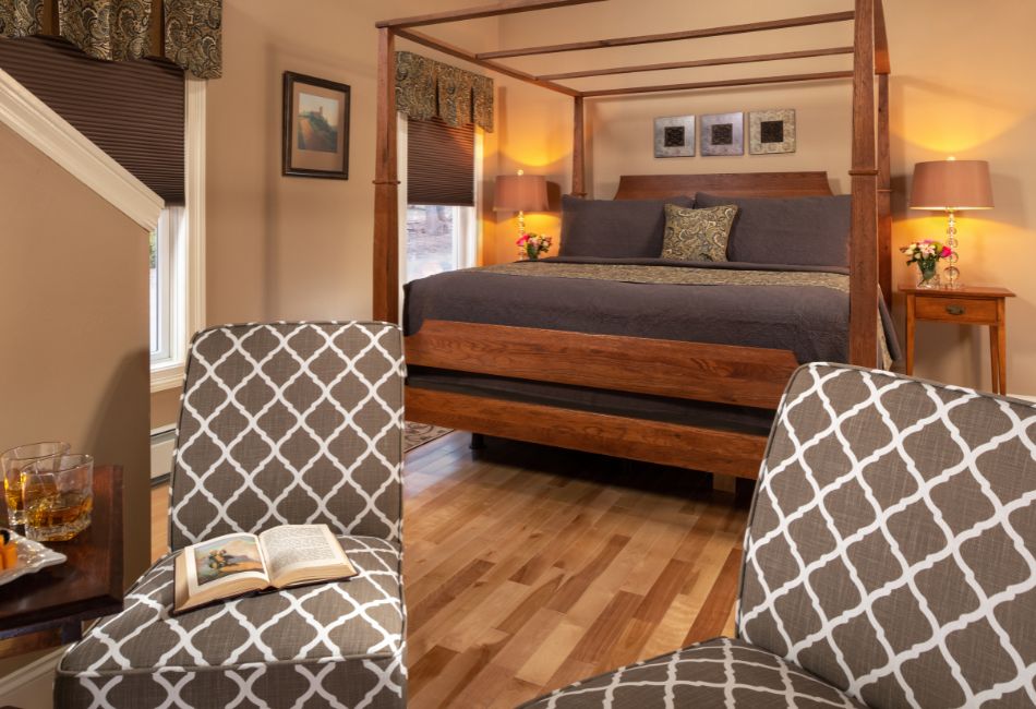 A cozy bedroom featuring a four-poster bed, two patterned chairs, and warm wooden accents.