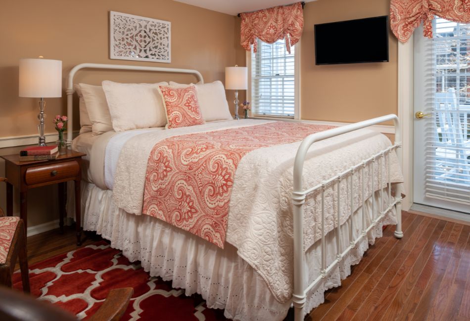 A neatly arranged bedroom featuring a white metal bed with decorative bedding, a wooden side table, and warm-toned walls.