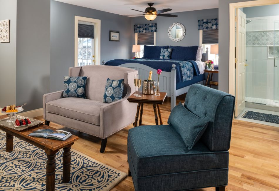A cozy, stylish hotel room featuring a seating area, a bed with blue bedding, and an adjoining bathroom.