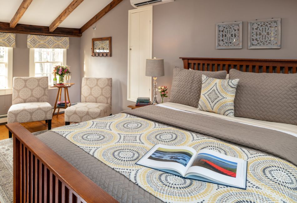 A cozy bedroom featuring a wooden bed, patterned bedding, and two chairs beside a small table with flowers.