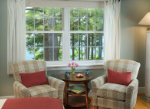 Cozy seating area by a window with views of trees and a small table holding a vase of flowers and two cups.