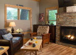Cozy living room with a stone fireplace, brown leather sofa, wooden chairs, and a coffee table set for breakfast.