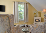 Cozy living space featuring two patterned armchairs, a small table with wine glasses, a TV, and a window with greenery visible outside.