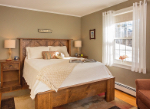 Cozy bedroom with a wooden bed, decorative pillows, bedside lamps, and a window with soft curtains.