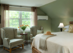 Cozy bedroom featuring a bed, two armchairs, and a vase of flowers by the window.