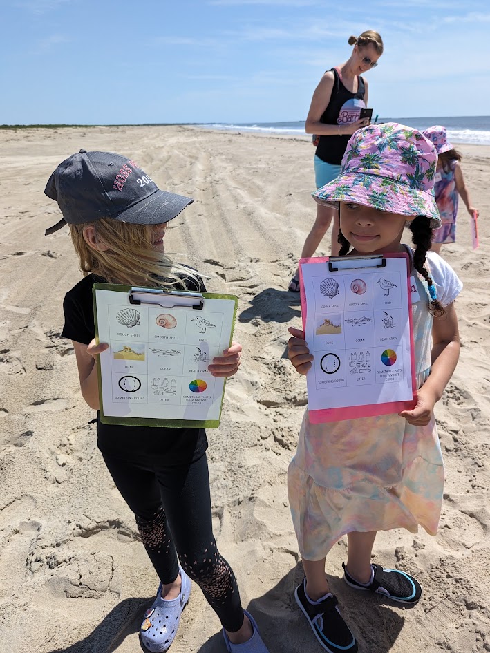 Two girls on the beach at Assateague with clipboards, working through a scavenger hunt on a Chincoteague Bay Field Station trip.