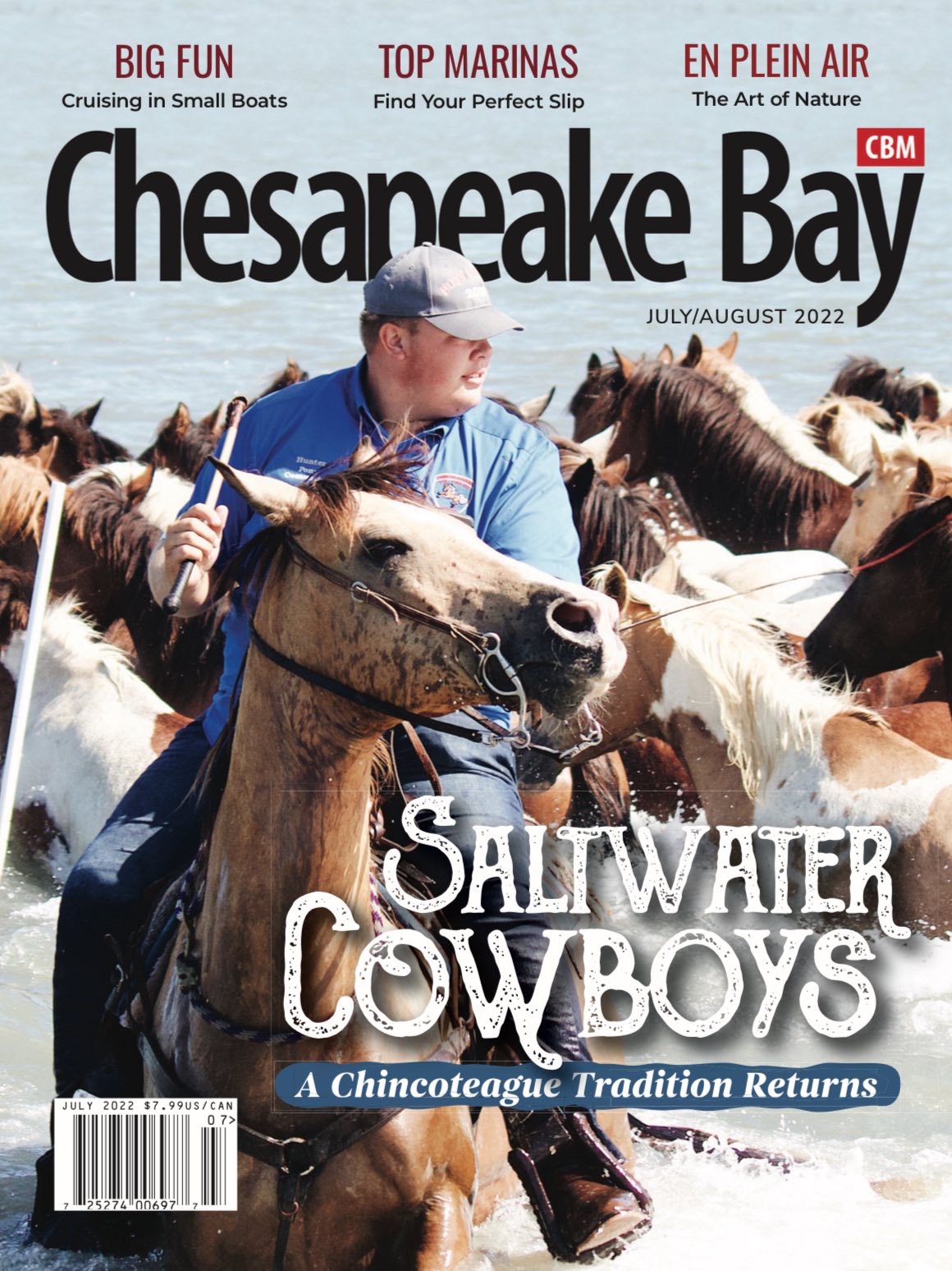 A man on horseback herds a group of horses through water, on the cover of Chincoteague magazine.