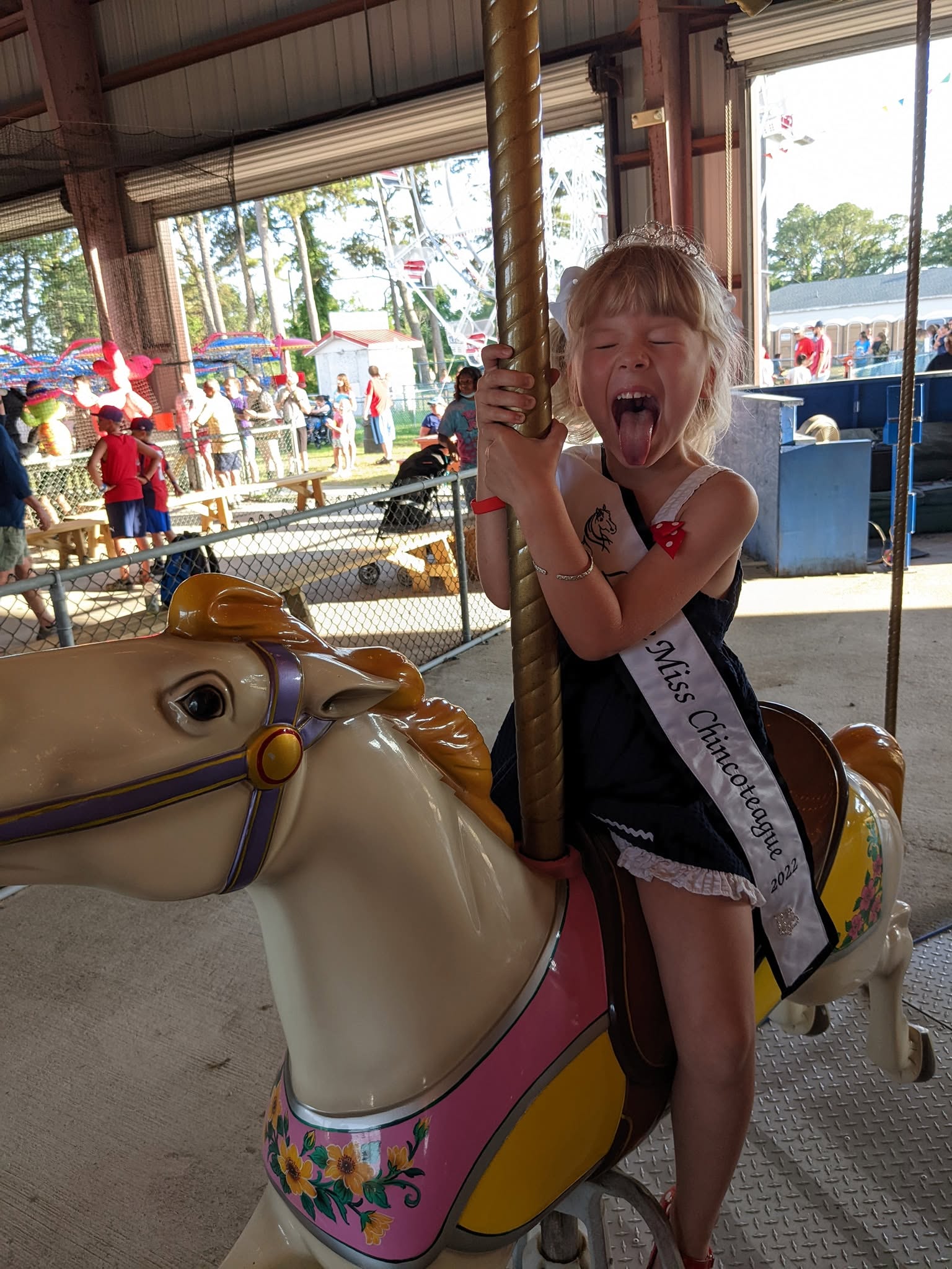 A girl riding the carousel at the Chincoteague Carnival, wearing a Miss Chincoteague sash.