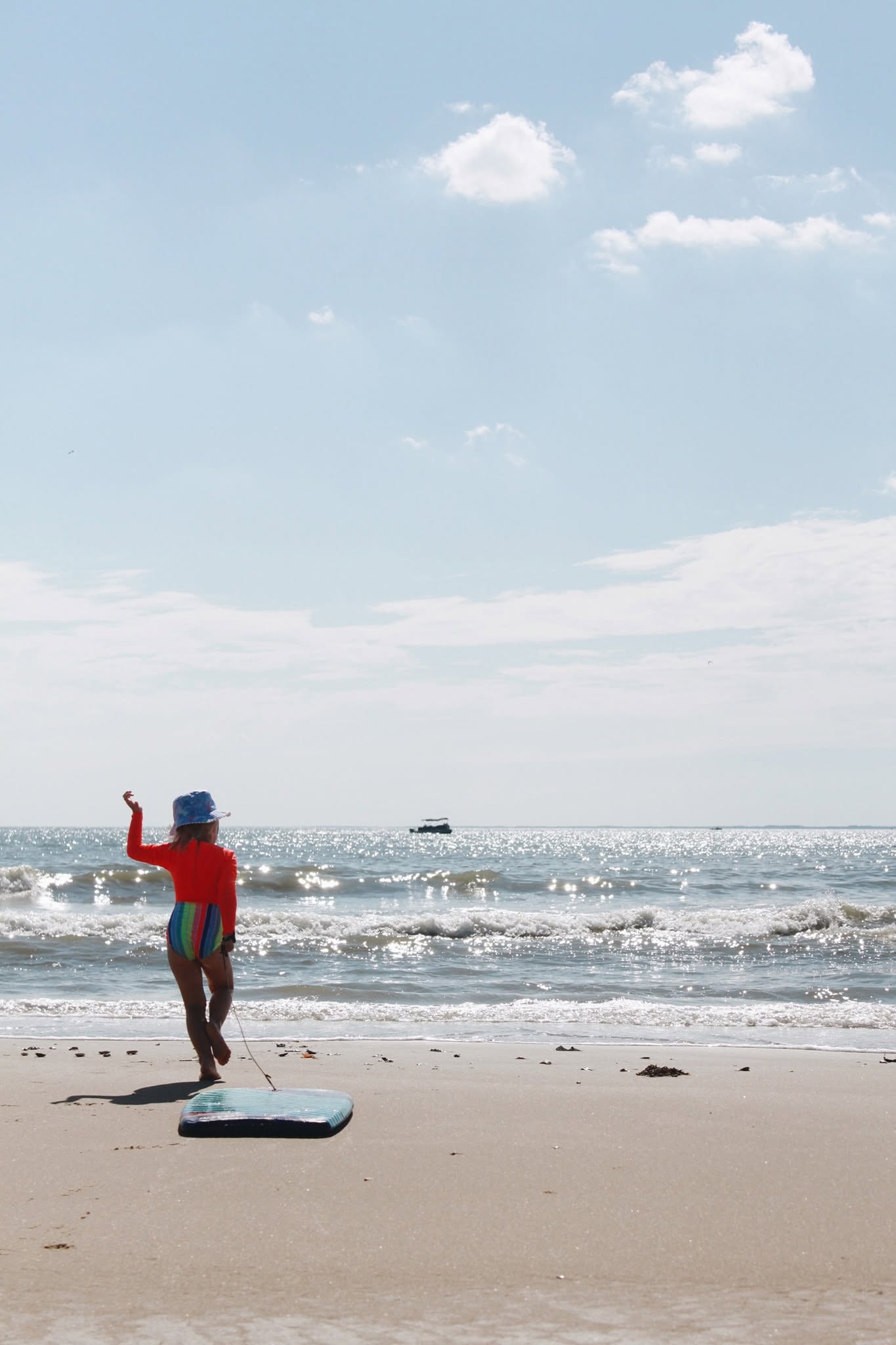 A child running down the empty beach at Assateague towards the surf, carrying a boogie board.