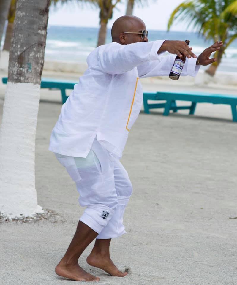 A man dancing and laughing on a sandy beach with a beer in his hand