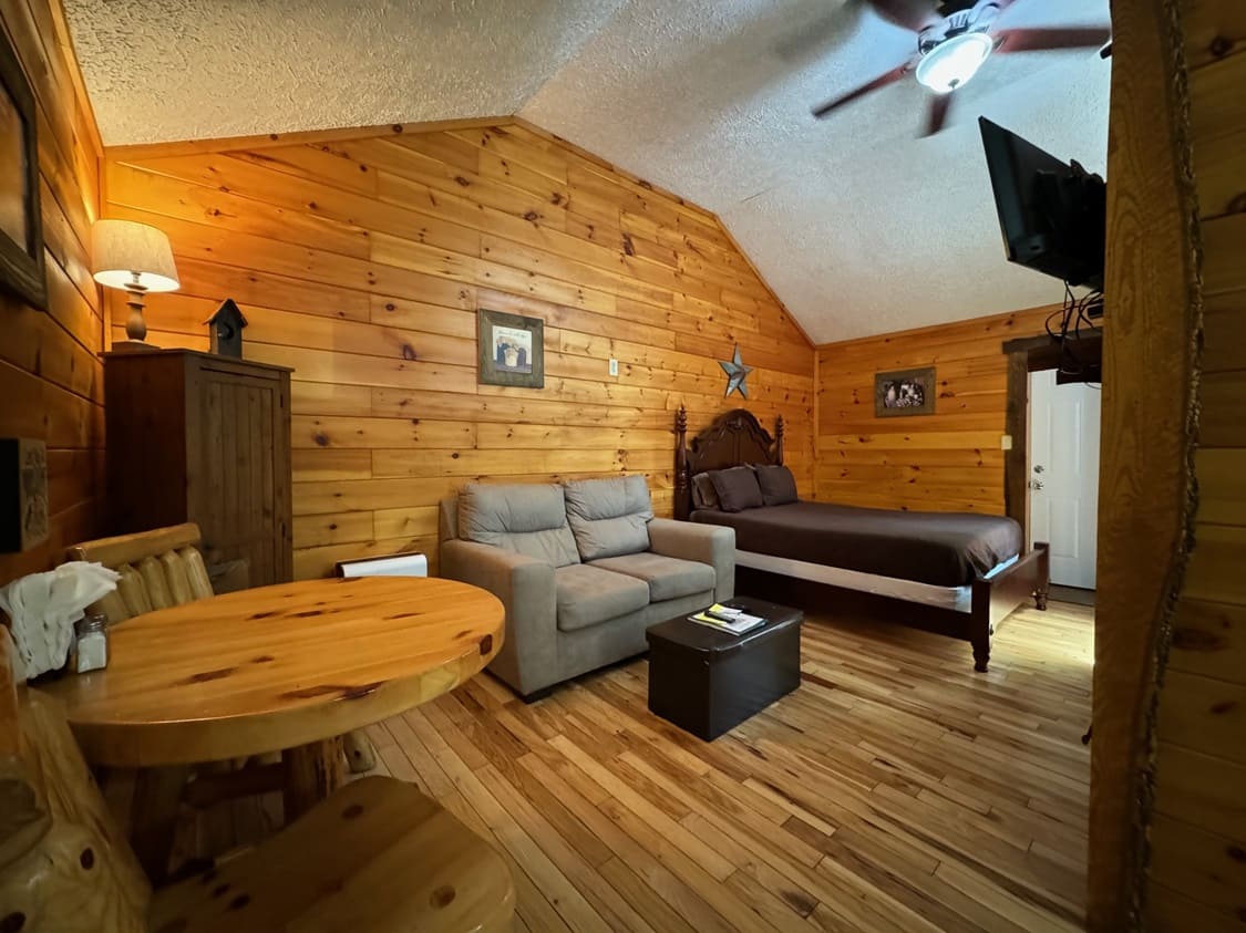 Cozy interior of a rustic cabin with wooden walls, a bed, a sofa, and a small dining table.