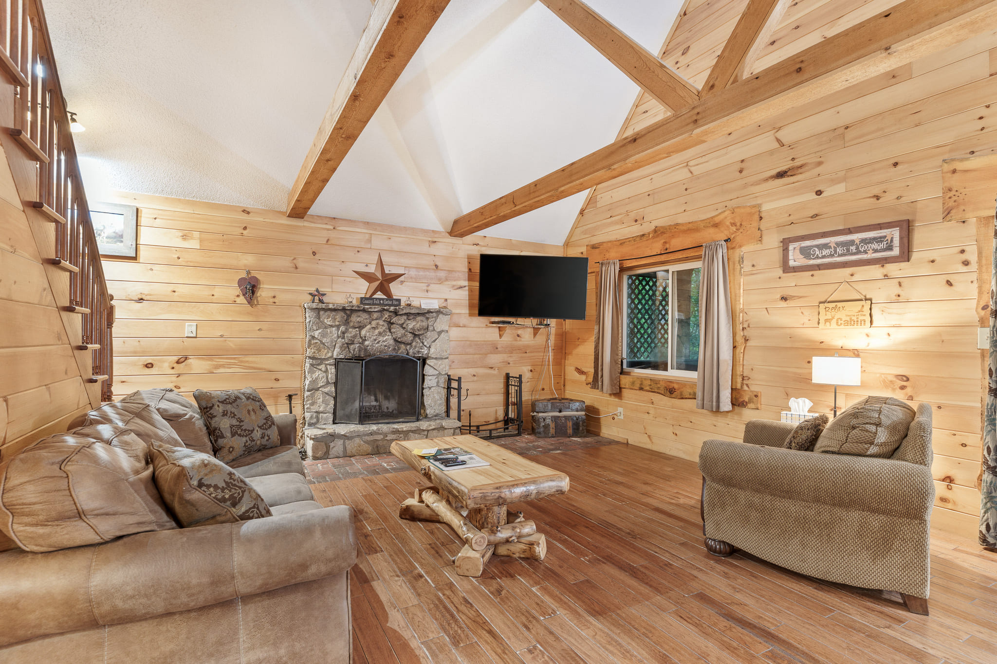 Cozy living room featuring wooden paneling, a stone fireplace, and rustic furniture.