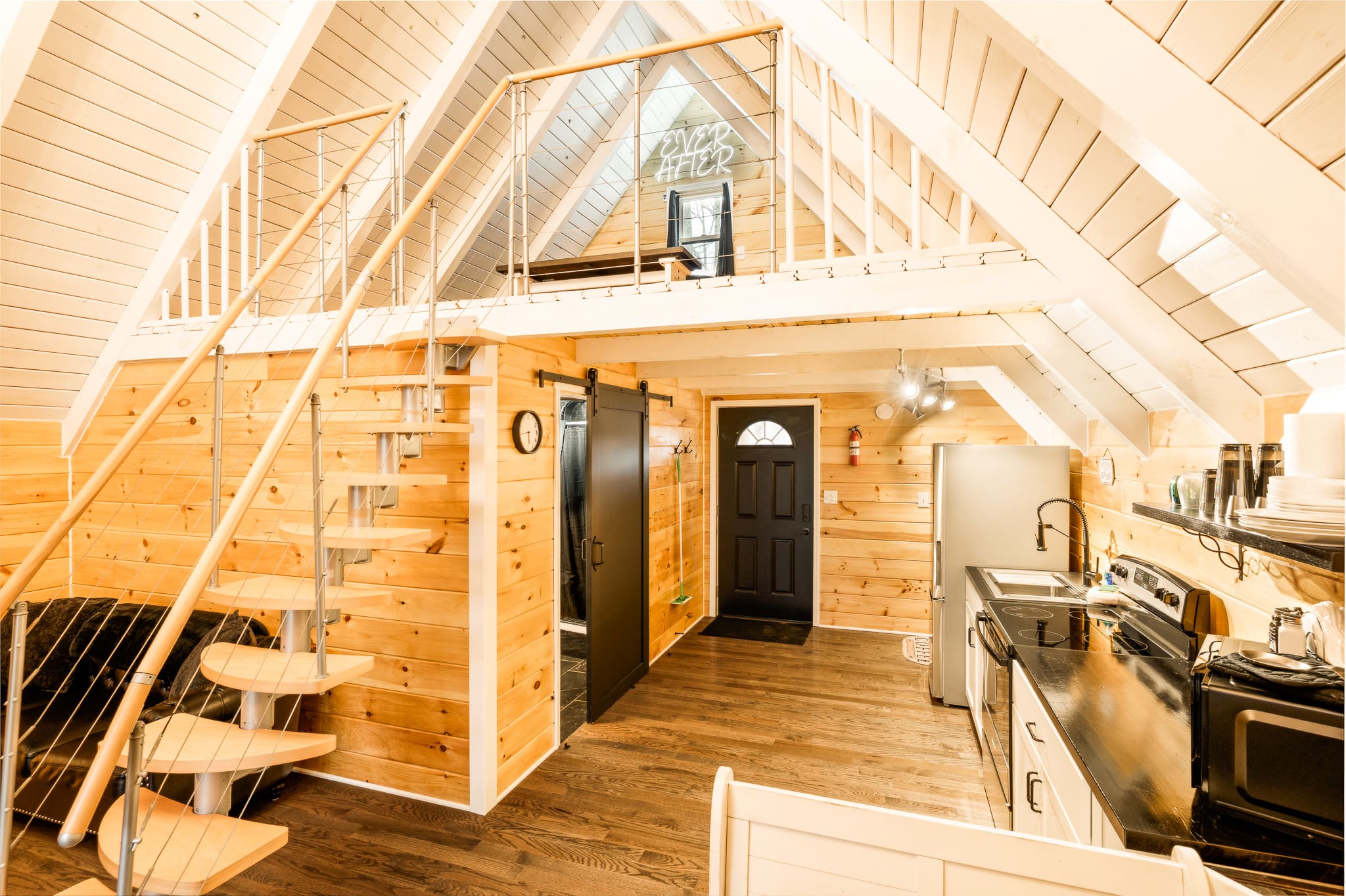 A cozy, wooden interior of a chalet featuring a spiral staircase, kitchen appliances, and a lofted area.