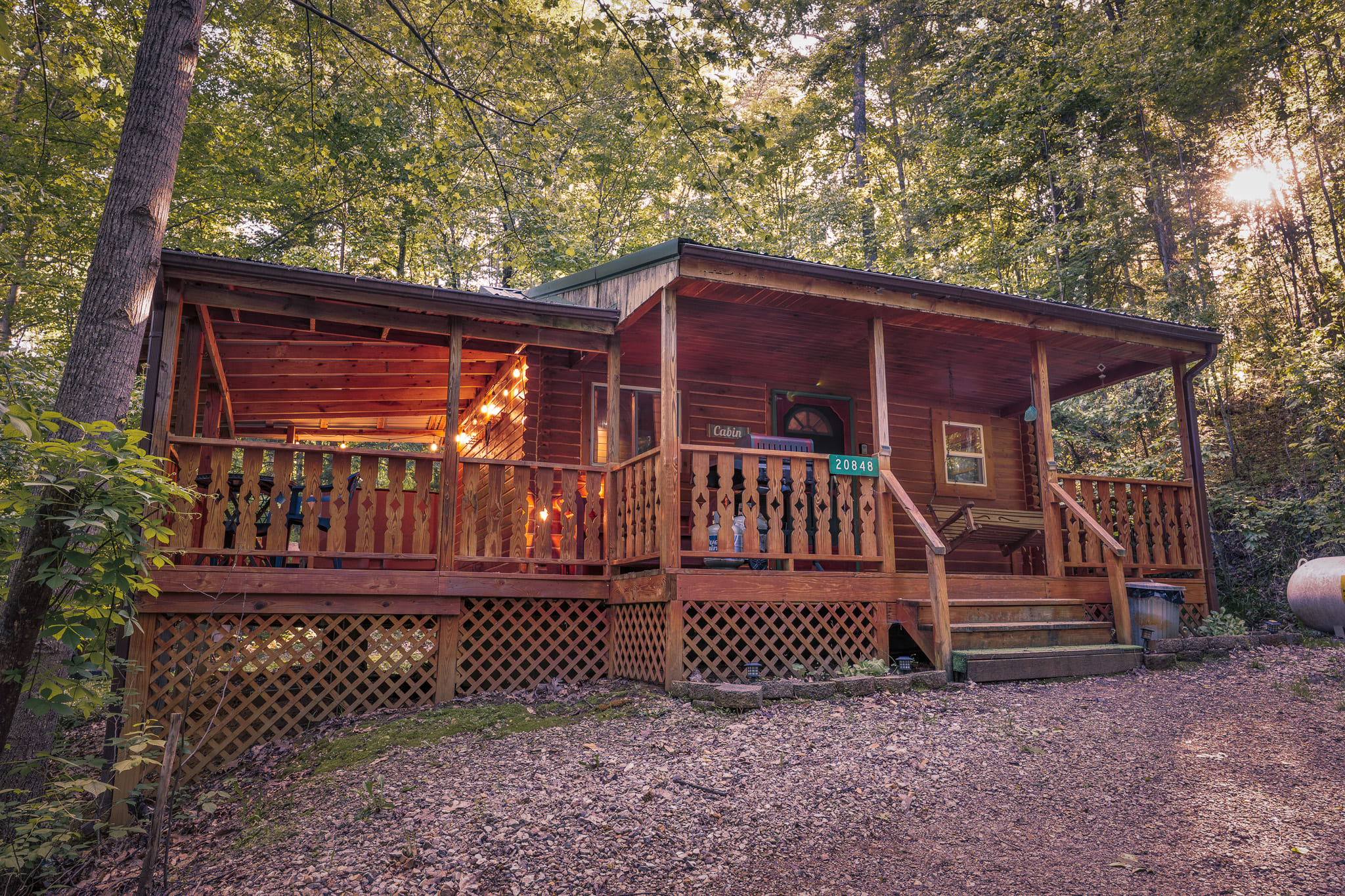 A cozy wooden cabin nestled in a wooded area, featuring a large porch and warm lighting.