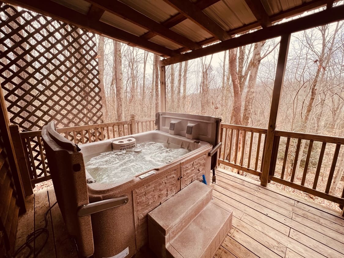A hot tub bubbles on a wooden deck surrounded by bare trees.