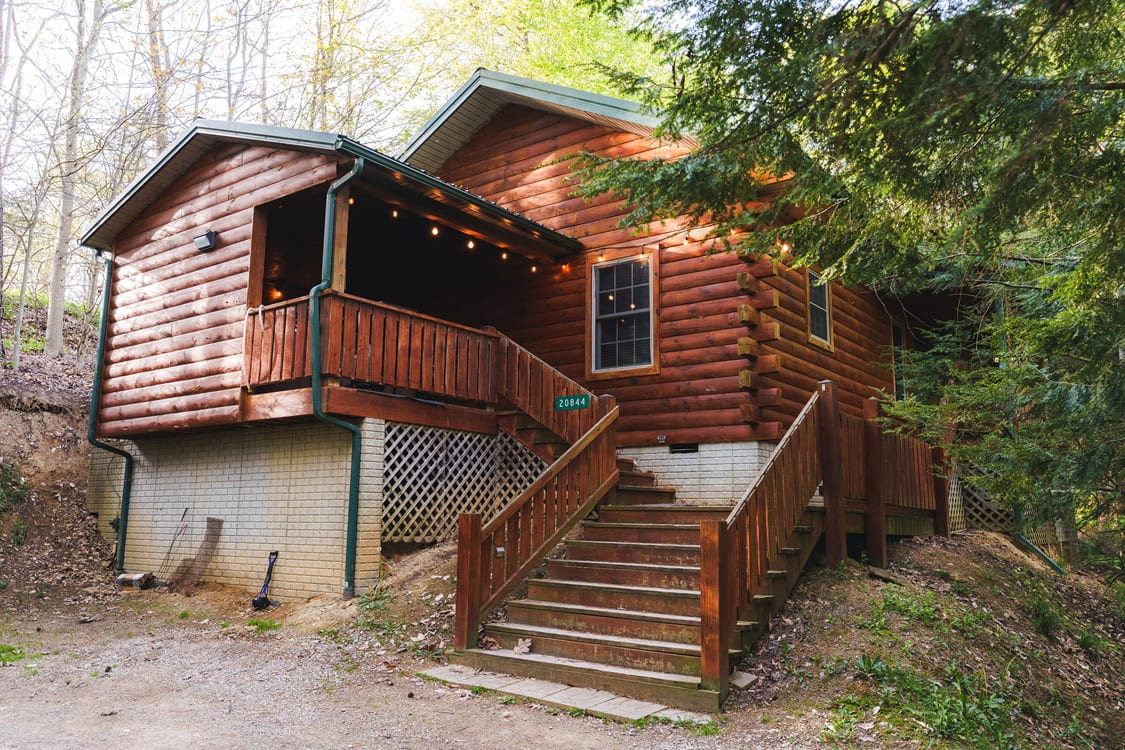 A charming log cabin with a porch and wooden steps, surrounded by trees.