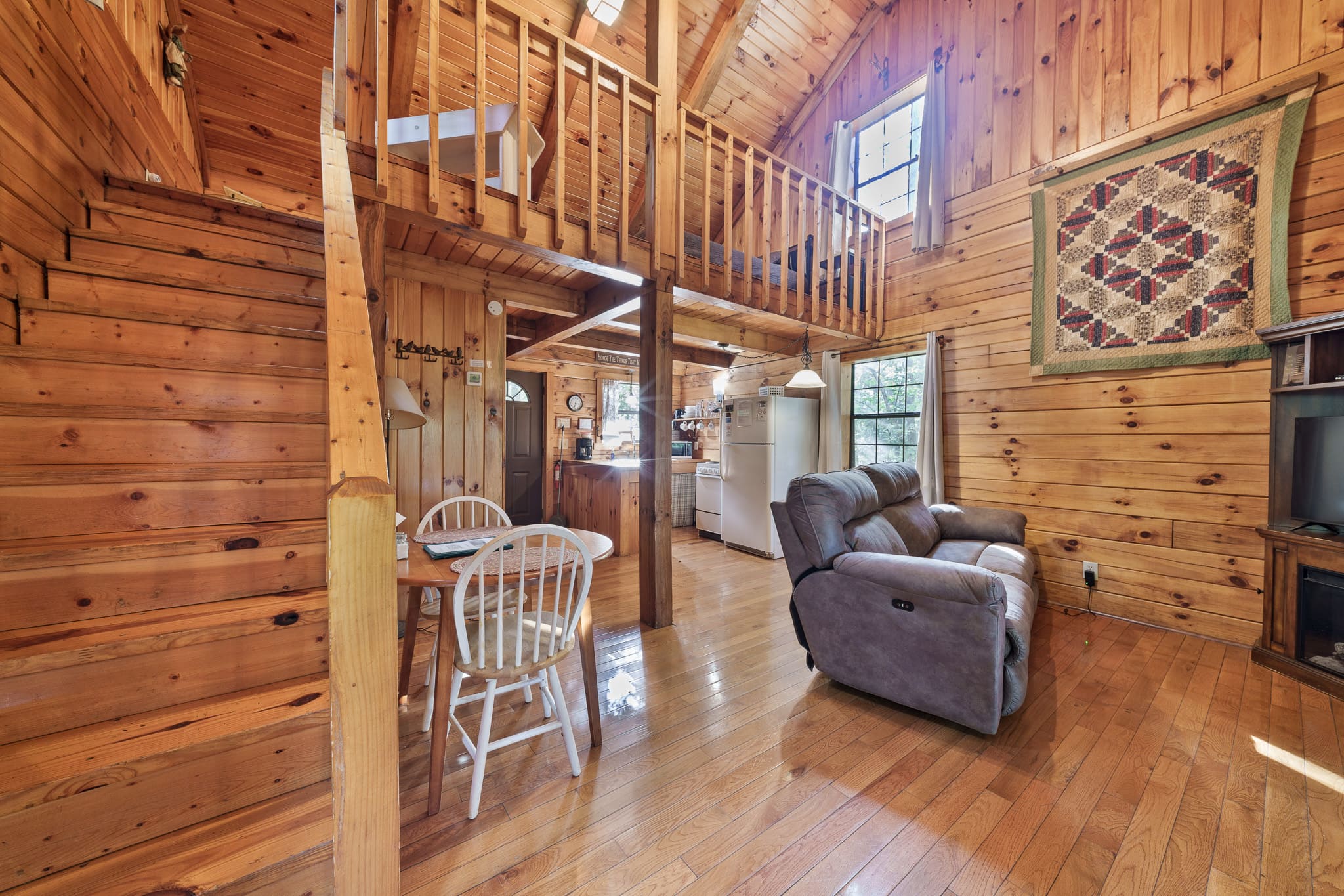 Cozy wooden interior of a cabin featuring a staircase, dining area, and plush seating.