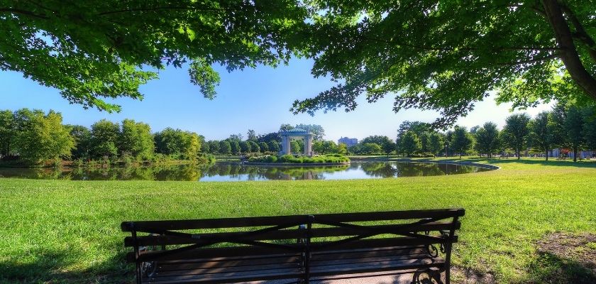 A park bench at Forest Park near St. Louis, MO, overlooking a pond and bandstand during summer.