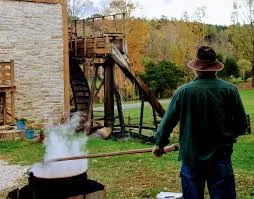 Man in green shirt over steaming pot of apple butter in front of stone flour mill Man in green shirt over steaming pot of apple butter in front of stone flour mill