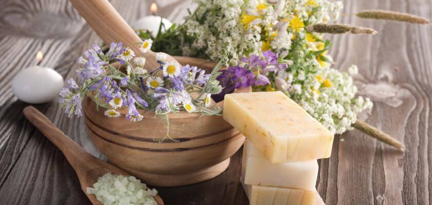 handmade soaps wildflowers and bath salts on a wooden table with candles in the background