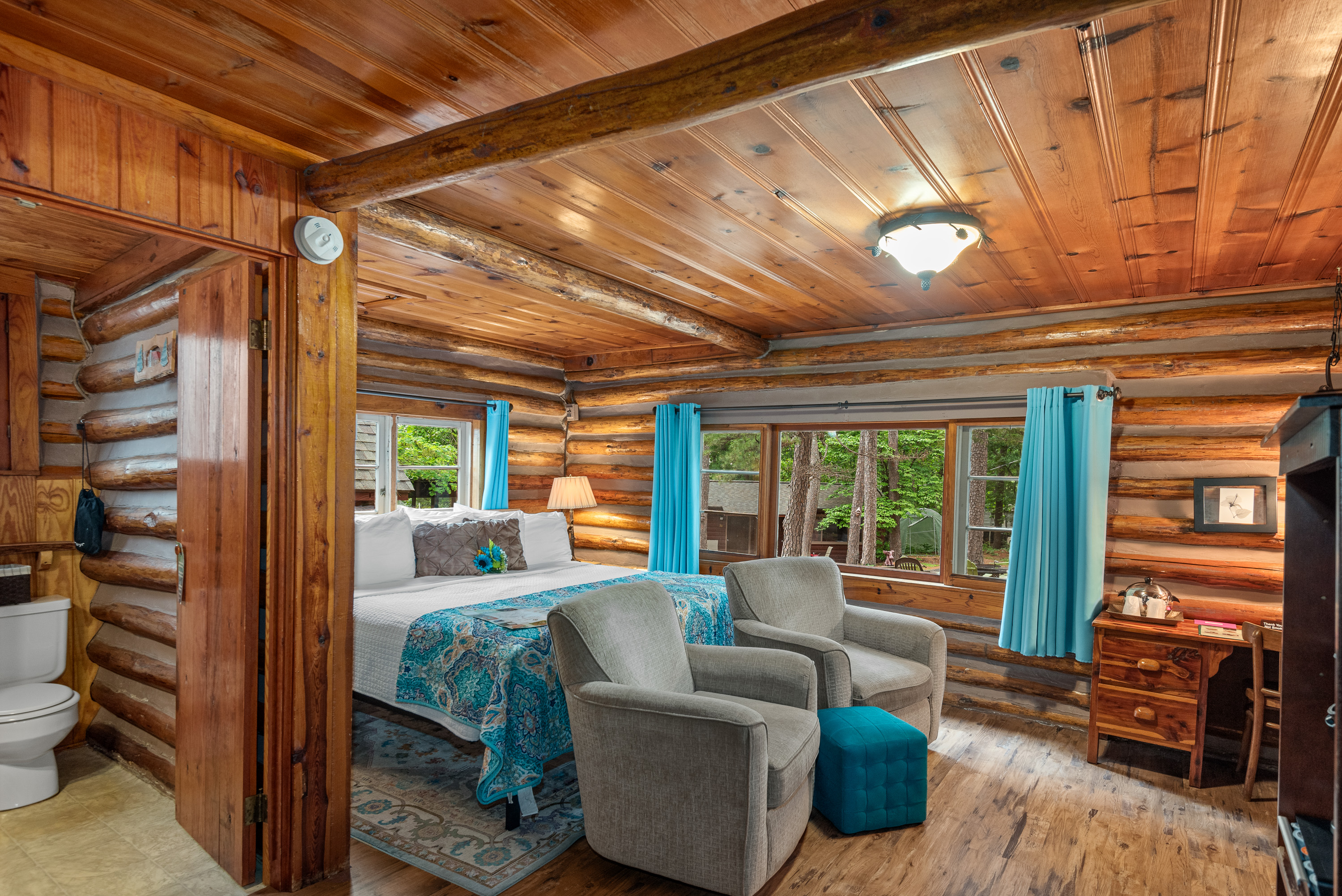 Log cabin showing wood frame bed and two rockers and curtains